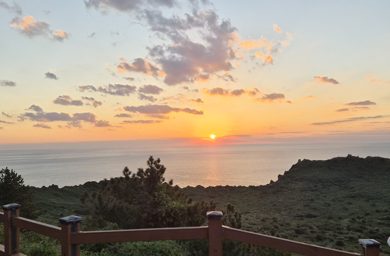 Sunrise over the sea beyond the summit railings at Seongsan Ilchulbong